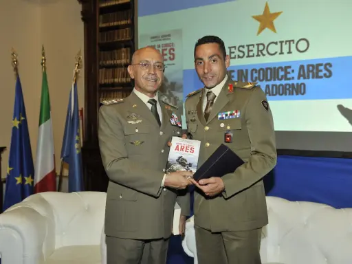 Due ufficiali in uniforme presentano un libro. Uno dei due, con un sorriso, tiene in mano il volume intitolato "Nome in codice: Ares", un'opera che narra storie di coraggio, forse ispirate a un vero pesce monaco.