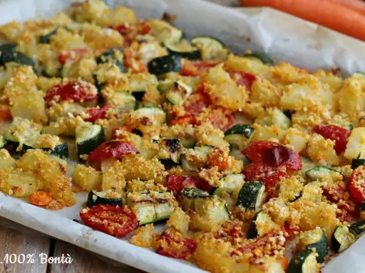 Un vassoio di verdure al forno, con patate, zucchine e pomodorini, condite con pangrattato dorato.