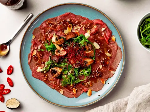 Rindercarpaccio mit Pilzen, Rucola und Mandeln. Eine köstliche Variation von Carpaccio, garniert mit Chili und Trüffel.