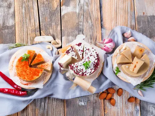 Drei runde Käsealternativen, eine mit Paprikapulver, eine mit roten Beeren und eine mit Kräutern, als cheddar ersatz arrangiert.