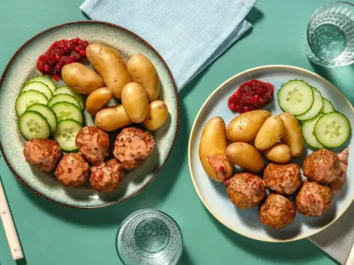 Två tallrikar med köttbullar, småpotatis, gurka och lingonsylt. En perfekt snabb middag för två.