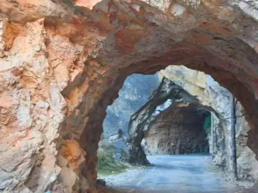 Un túnel natural en la ruta del silencio Teruel, con paredes de roca rojiza y un camino que se adentra en la montaña.