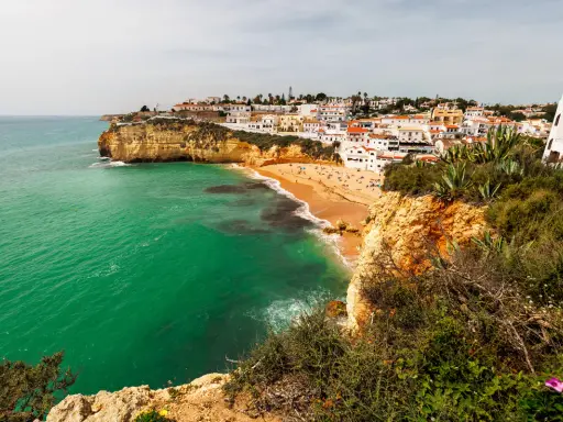 Blick auf die sonnenverwöhnte **Carvoeiro Altstadt** mit ihren weißen Häusern, die sich an die Klippen schmiegen. Der goldene Sandstrand lädt zum Verweilen ein, während das smaragdgrüne Meer sanft an die Küste brandet.