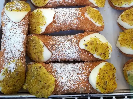 Chrupiące rurki z kremem, posypane cukrem pudrem i pistacjami, kuszą swoim wyglądem.