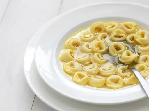 Tortellini in brodo, uno dei cibi tipici dell'Emilia Romagna, serviti in una ciotola bianca con un cucchiaio.