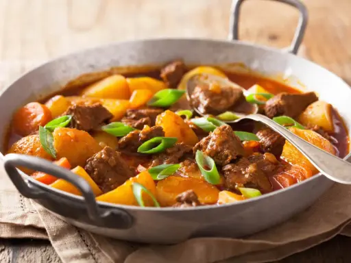 Un reconfortante estofado de ternera con patatas y zanahorias, adornado con cebolleta verde.