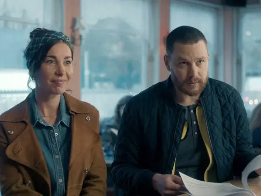 En kvinna med scarf och en man med skägg sitter vid ett bord. De ser ut att vara med i en dansk serie på SVT.