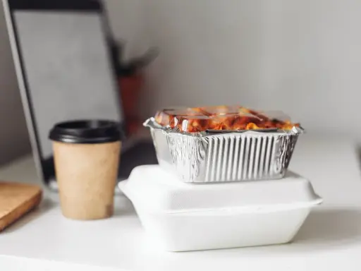 Gotowe jedzenie na wyjazd: zapiekanka w folii aluminiowej i kawa w kubku. Idealne na szybki lunch przy laptopie.