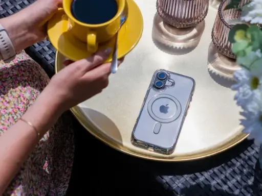 Eleganckie etui przezroczyste z wzorami na telefon, leżące obok żółtej filiżanki kawy i białych kwiatów.