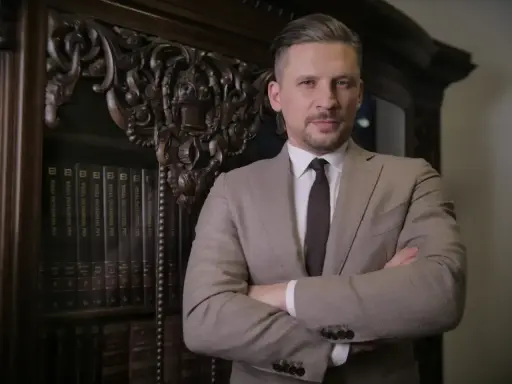 Mężczyzna w garniturze stoi przed regałem z książkami prawniczymi.