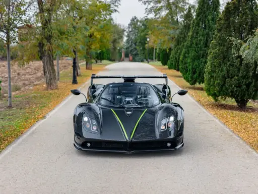 Czarny Pagani Zonda z zielonym akcentem na masce, zaparkowany na alei. Jego cena jest astronomiczna.