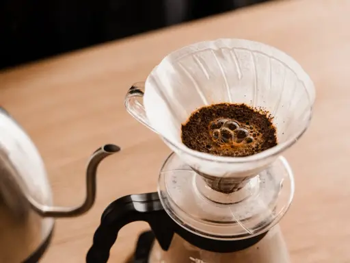 Frisch aufgebrühter Kaffee blubbert im Papierfilter. Ein Wasserkocher steht bereit, um das Ritual des Kaffeefilter selber machen zu beginnen.