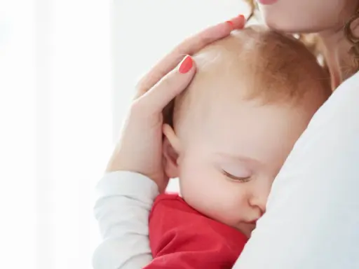Ciemiączko przednie niemowlęcia delikatnie dotykane przez matkę. Dziecko śpi wtulone w jej ramię.