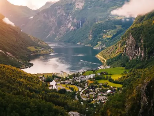 Majestätisk natur i Norge med en djup fjord, branta berg täckta av grönska och ett litet samhälle vid vattnet.