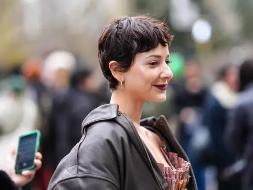 Frau mit einem lässigen Pixie-Cut, dunklem Lippenstift und Lederjacke lächelt in die Kamera.