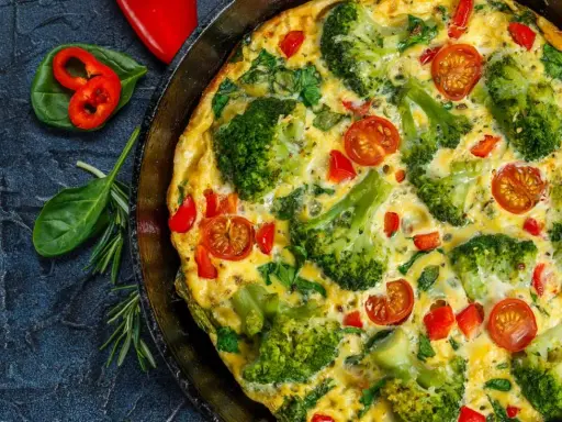 Pyszny omlet na słono z brokułami, pomidorkami i papryką, podany w patelni.