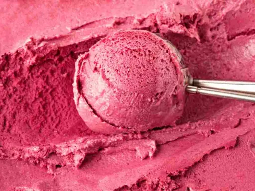 Un cucchiaio raccoglie una porzione di cremoso gelato fatto in casa, dal colore rosa intenso, su uno sfondo dello stesso dolce freddo.