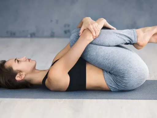 Frau in Yoga-Pose, Knie zur Brust gezogen. Ein Geheimtipp bei Ischias zur Linderung von Rückenschmerzen.