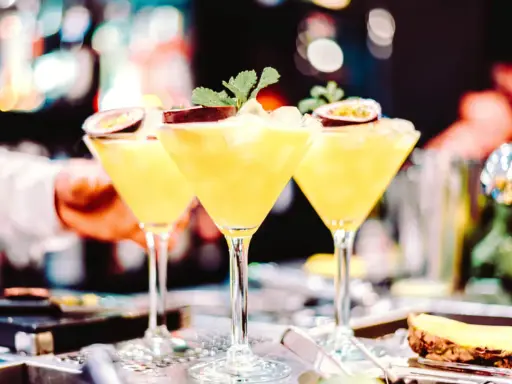 Trzy kieliszki z orzeźwiającą mango margarita, ozdobione połówkami marakui i listkami mięty, gotowe do podania.