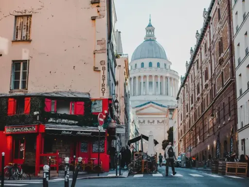 Urokliwa uliczka w paryskiej dzielnicy łacińskiej z czerwonym bistro i majestatycznym Panteonem w tle.