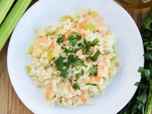 Pyszne risotto z krewetkami, udekorowane natką pietruszki, obok łodygi selera i oliwy.