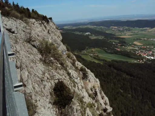 Widok z **Hohe Wand** na dolinę z lasami i wioskami. Stroma, skalista ściana po lewej stronie.