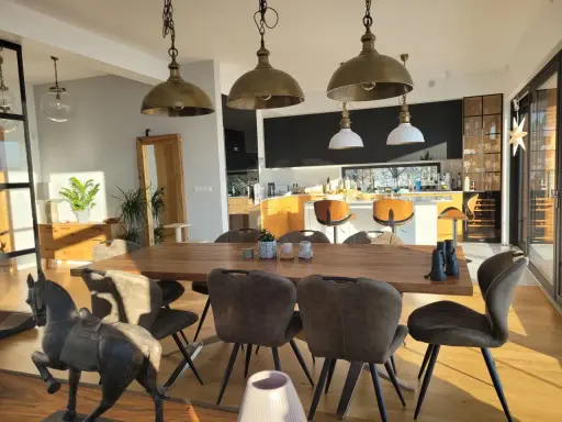 Oświetlenie salonu inspiracje: industrialne lampy wiszące nad drewnianym stołem, nowoczesna kuchnia w tle.