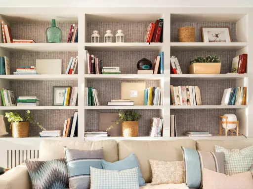 Estanterías blancas llenas de libros, plantas y objetos decorativos. Una idea de **qué poner detrás del sofá** para crear un rincón acogedor y lleno de estilo.