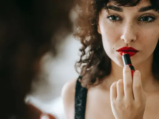 Donna con capelli ricci applica un trucco con rossetto rosso vibrante, creando un look audace e seducente.