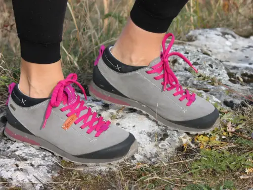 Szare buty trekkingowe Aku Bellamont z jaskrawymi, różowymi sznurówkami na kamienistym, trawiastym podłożu.