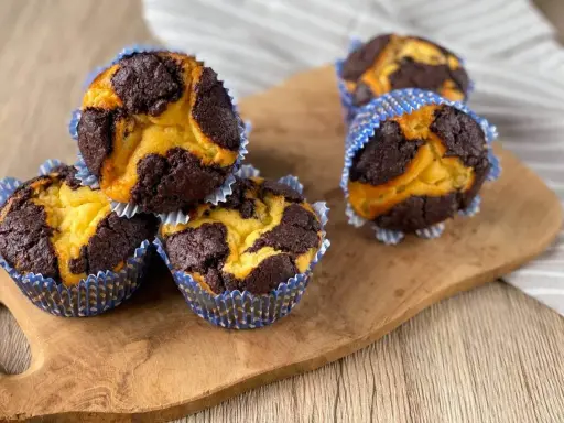 Schokoladen-Vanille-Zupfkuchen-Muffins in blauen Papierförmchen auf einem Holzbrett.