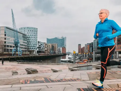 Frau mit kurzen Haaren läuft im Hafen. Sie trägt Sportkleidung und Schuhe. Mit Laufen abnehmen ist ihr Ziel.