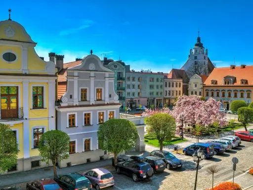Kolorowy rynek w Kluczborku z zabytkowymi kamieniczkami, kwitnącą magnolią i wieżą kościelną. Kluczbork atrakcje zachwycają.