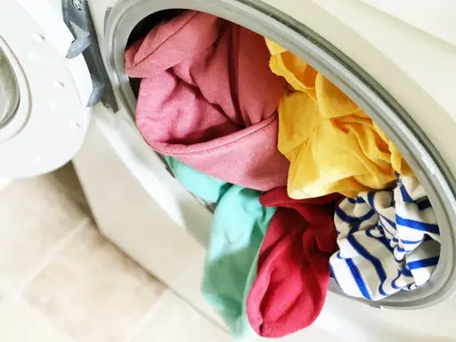 Carga de lavadora con ropa de colores variados, incluyendo rosa, amarillo, turquesa y rayas azules. ¡A ver si se puede lavar ropa blanca con ropa de color sin problemas!