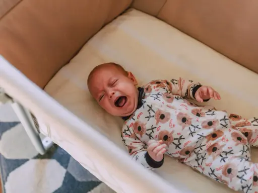 Bebé llorando en su cuna, con un pijama de koalas. Un momento difícil para dejar llorar a un niño de 2 años para dormir.