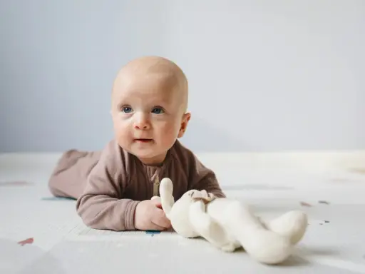 Söt bebis på mage med en mjuk kanin. Bebis mage storlek verkar perfekt för lek och utforskning.