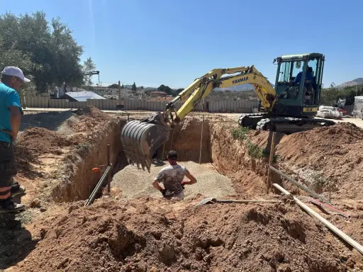 Excavadora amarilla trabajando para cavar zanjas en un día soleado. Un hombre supervisa la obra.