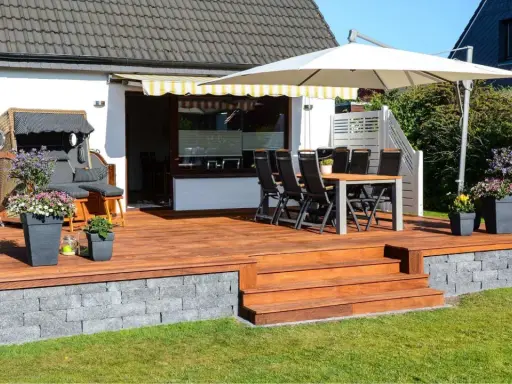 Eine schöne garten terrasse mit Holzdielen, Sitzmöbeln, Sonnenschirm und Blumen. Perfekt für entspannte Stunden im Freien.
