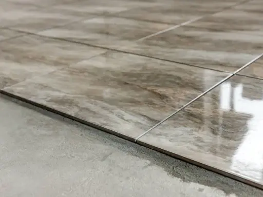 Detalle de las partes de un piso: baldosas de cerámica con veteado marrón y gris, recién colocadas sobre una base de cemento.