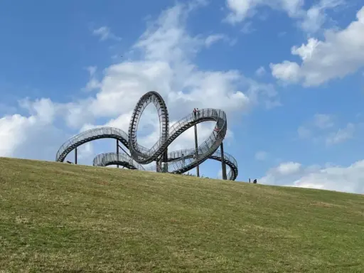 Ein skulpturales Kunstwerk auf einem Hügel, das an eine Achterbahn erinnert. Perfekt für spannende Ausflugsziele mit Kindern.