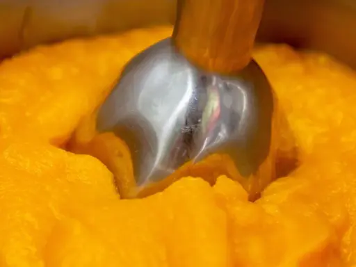 Metalowa końcówka blendera zanurzona w gęstym, pomarańczowym puree z dyni.