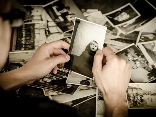 Ręce przeglądają stare fotografie, tworząc osobistą archiwizację zdjęć. Widać portret dziecka i grupowe ujęcia.