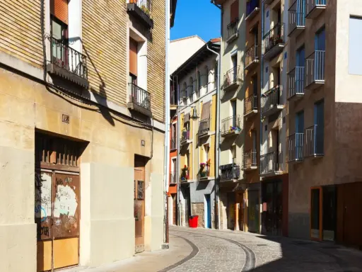 Calle adoquinada con edificios coloridos y balcones. Un cartel de "haya real estate" podría estar en uno de estos locales.