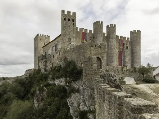 Die Obidos Burg thront majestätisch auf einem Felsen. Fahnen mit dem Namen "Obidos" wehen im Wind.
