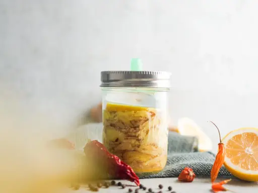 Ein Glas mit Ingwer fermentieren, daneben Zitronenscheiben und Chilis.