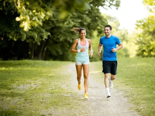 Ein lachendes Paar joggt glücklich durch einen sonnigen Park. Sie genießen die frische Luft und die Bewegung – das ist, was Joggen bringt.