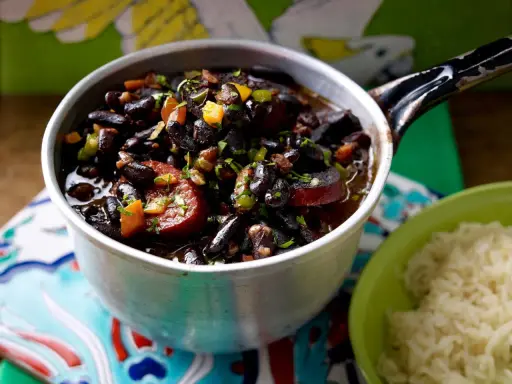 Herzhaftes schwarze bohnen rezept im Topf, mit Wurst und Gemüse, daneben eine Schüssel Reis.
