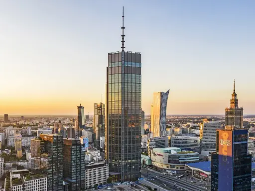 Warszawski krajobraz zdominowany przez wieżowce, w tym najwyższy hotel w Warszawie, lśni w złotym świetle zachodzącego słońca.