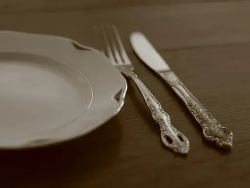 Une assiette blanche et des couverts en métal argenté, prêts pour un repas. L'art de nettoyer des couverts en métal argenté pour qu'ils brillent.