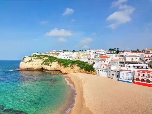 Traumhafte Küstenlandschaft in Portugal, Carvoeiro: Weiße Häuser schmiegen sich an grüne Klippen, daneben ein goldener Sandstrand und türkisfarbenes Meer.